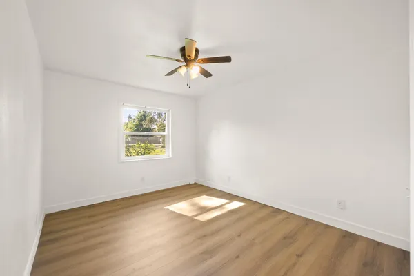 an empty room with wooden floor fan and windows