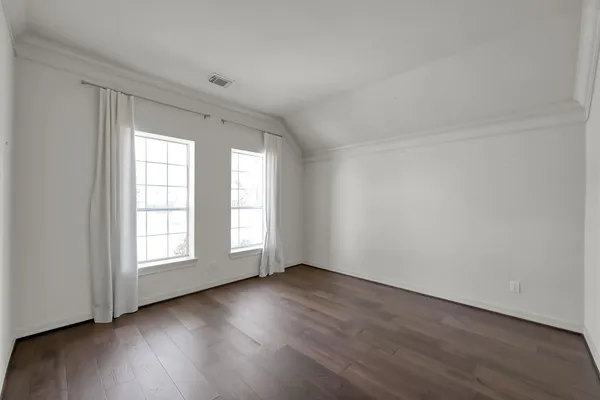 an empty room with wooden floor and windows with curtains