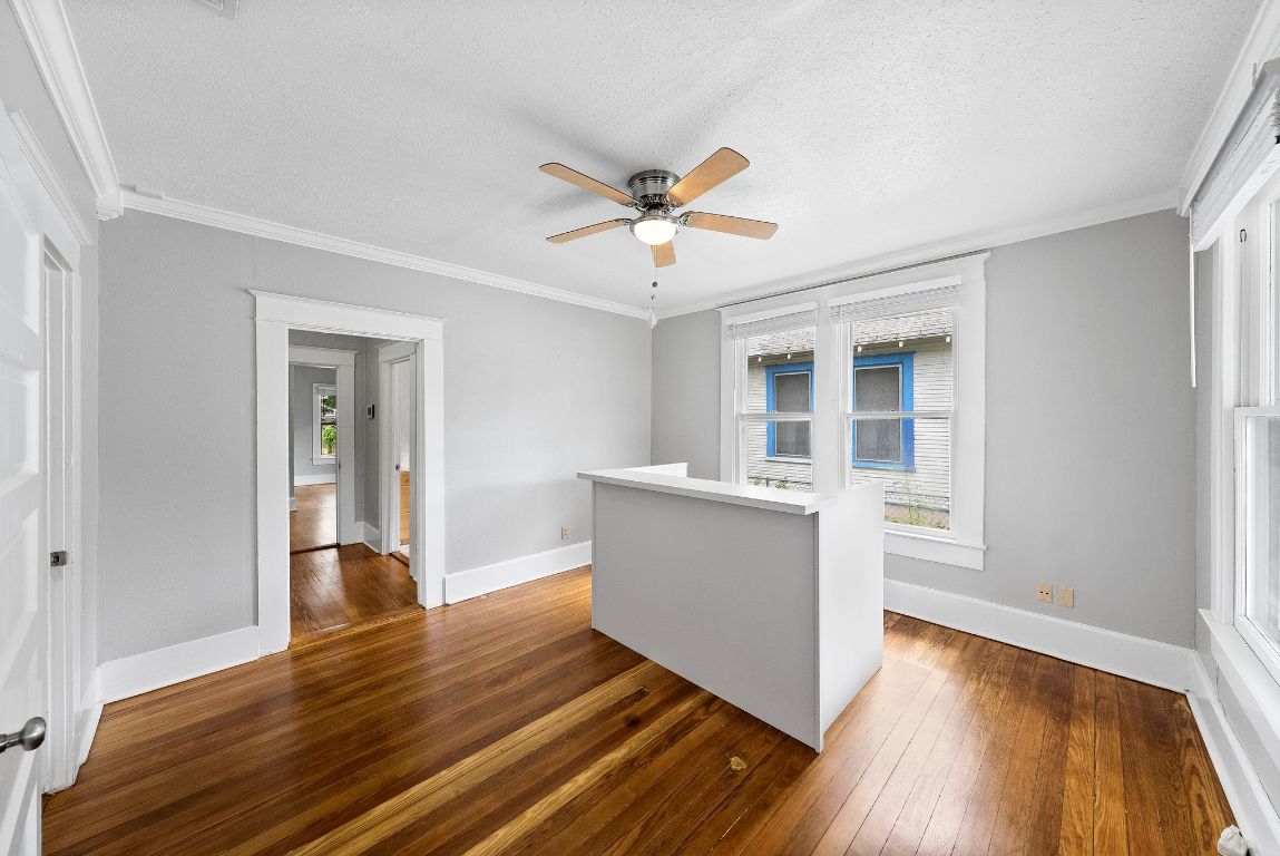 2032 East Cesar Chavez Street Austin, TX 78702 - Photo 2 of 25 Empty room featuring ceiling fan, dark wood-style flooring, baseboards, ornamental molding, and a textured ceiling