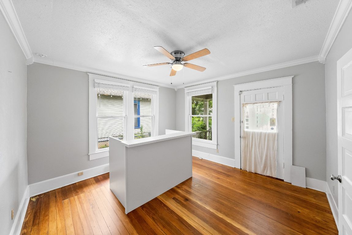 2032 East Cesar Chavez Street Austin, TX 78702 - Photo 4 of 25 Empty room with a textured ceiling, crown molding, hardwood / wood-style floors, a ceiling fan, and baseboards