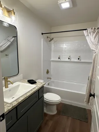 a bathroom with a granite countertop bathtub shower sink vanity and toilet