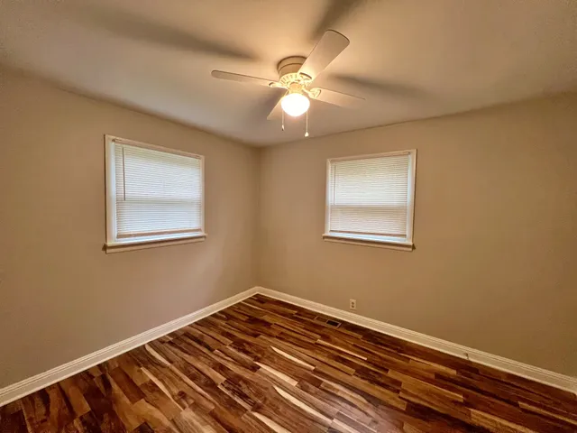 a view of an empty room with wooden floor and a ceiling fan