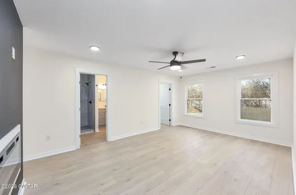 an empty room with wooden floor ceiling fan and windows