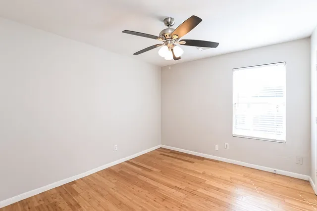 an empty room with wooden floor fan and windows