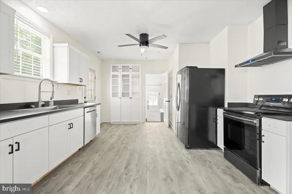 a kitchen with granite countertop a refrigerator oven a sink dishwasher and white cabinets with wooden floor