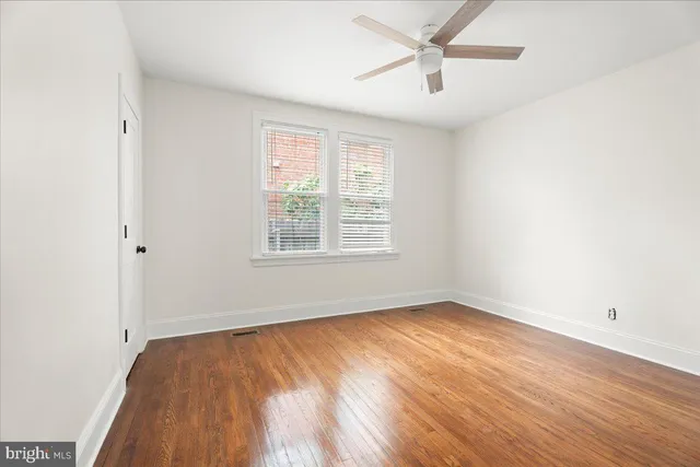 an empty room with wooden floor ceiling fan and windows