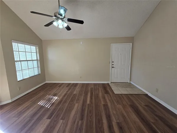 an empty room with wooden floor chandelier fan and windows