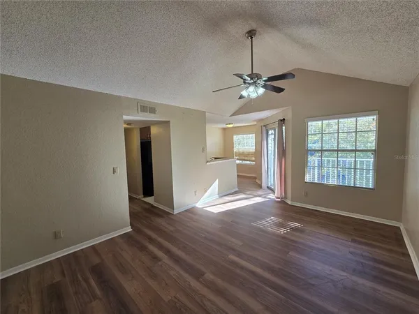 an empty room with wooden floor chandelier fan and windows