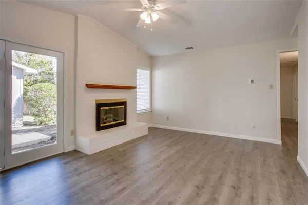 an empty room with wooden floor fireplace and windows