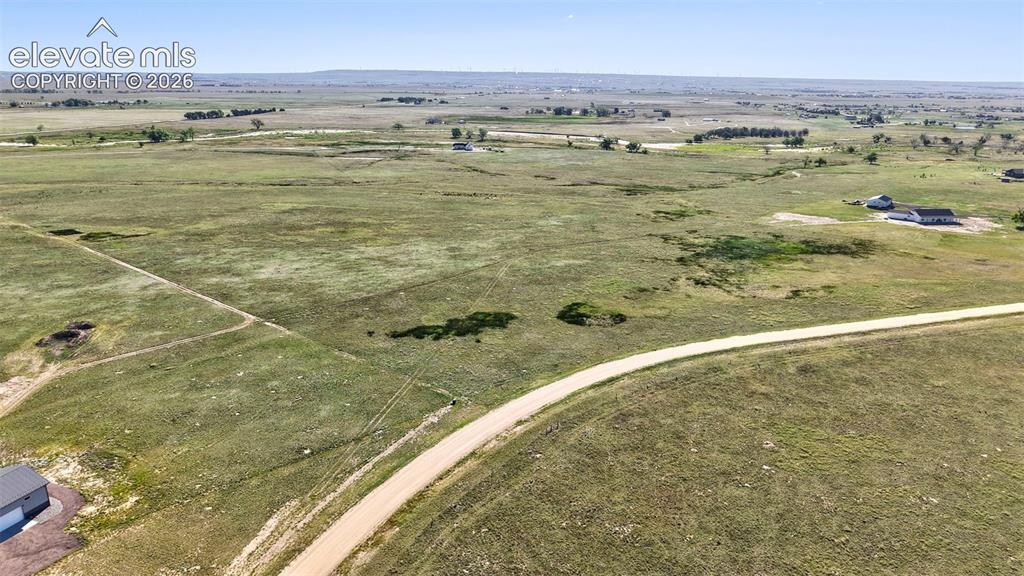 8007 Wrangler Ranch View Peyton, CO 80831 - Photo 5 of 9 Expansive grassland property featuring a gravel road, distant homes, scattered trees, and a distant building with a dark roof and light siding