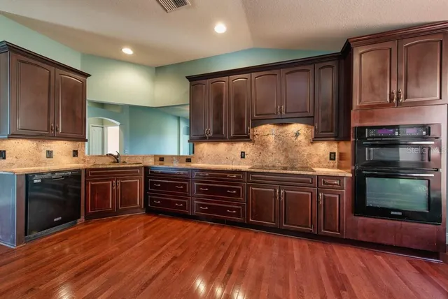 a kitchen with stainless steel appliances granite countertop wooden floors wooden cabinets and sink