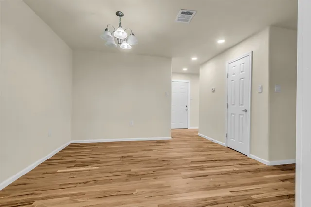 a view of an empty room with wooden floor and chandelier