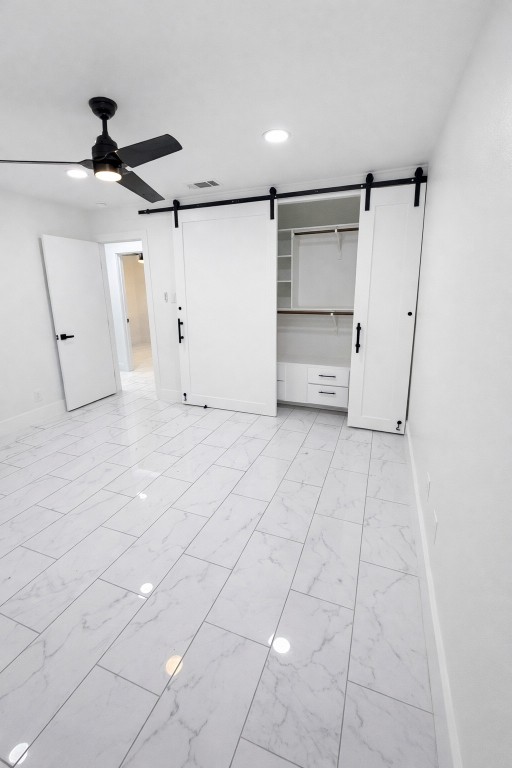 2014 Pecan Street Bastrop, TX 78602 - Photo 8 of 13 Unfurnished bedroom with a barn door, light marble finish floors, recessed lighting, and a ceiling fan