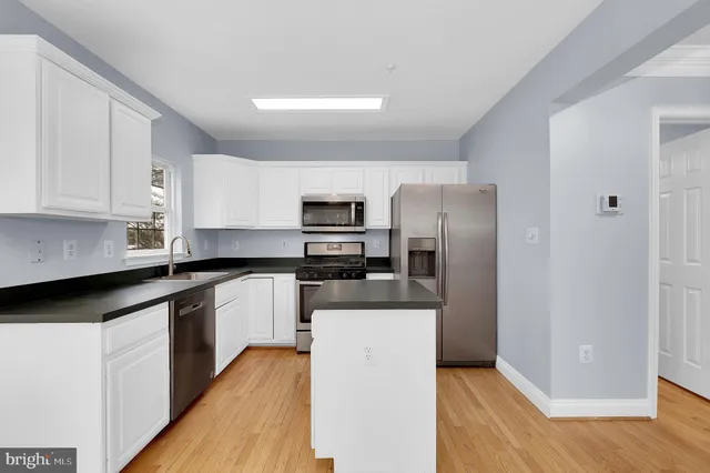 a kitchen with stainless steel appliances granite countertop a refrigerator a stove a sink and white cabinets with wooden floor