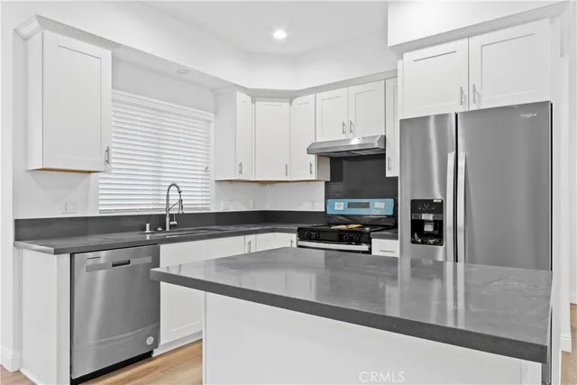 a kitchen with granite countertop a refrigerator a sink a stove and cabinets