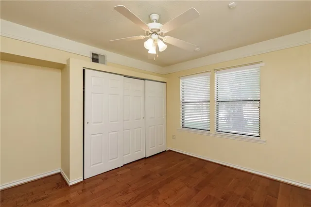 an empty room with wooden floor chandelier fan and windows
