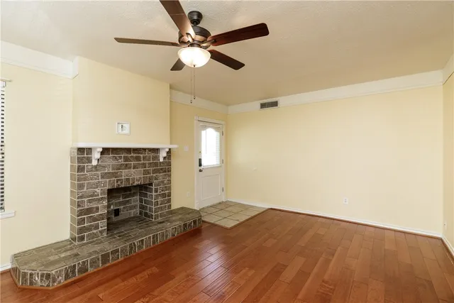 an empty room with wooden floor fireplace and windows