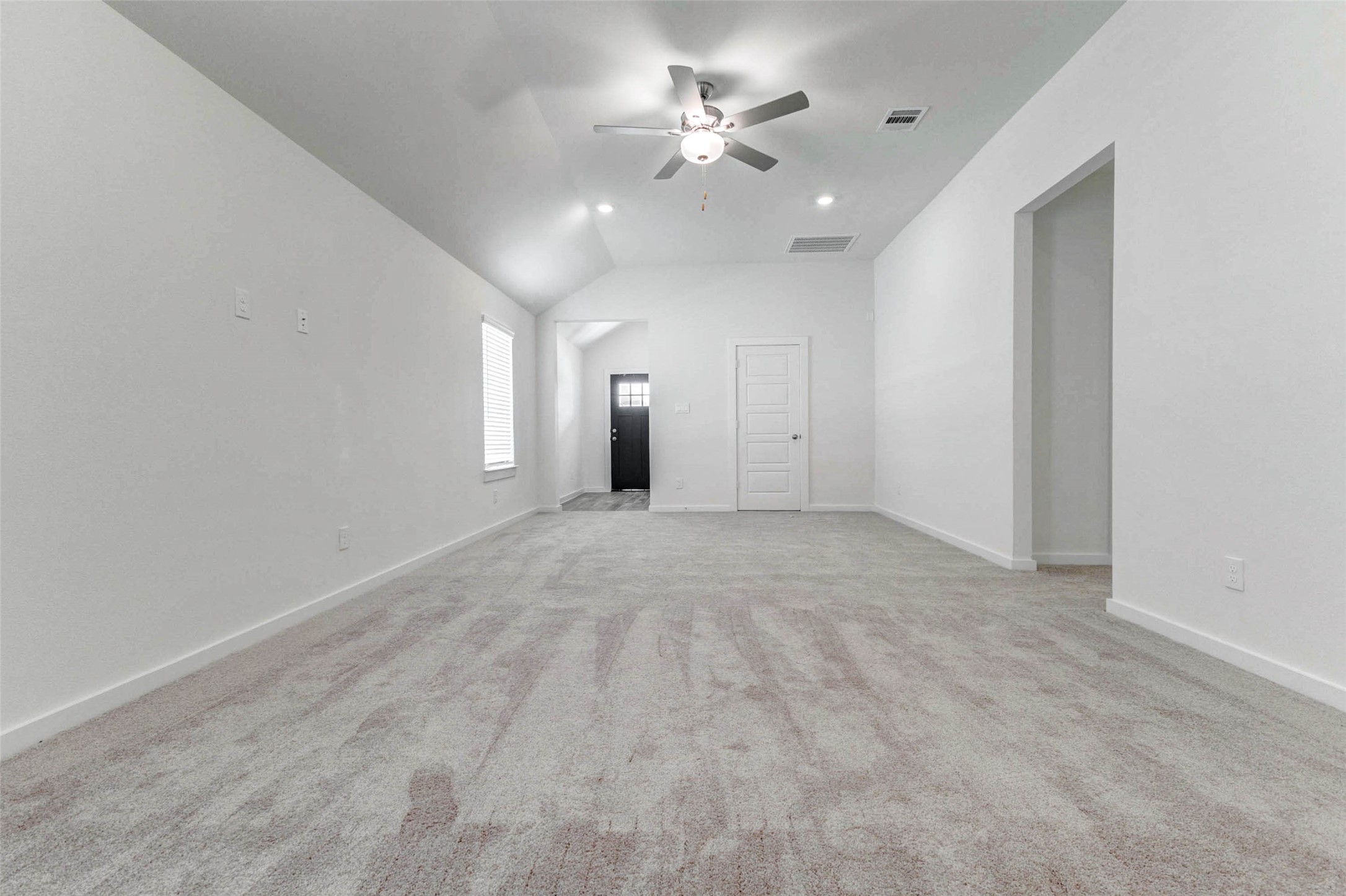 6475 Escondido Drive Rosharon, TX 77583 - Photo 12 of 32 Another view of the living area highlights the impressive ceiling height, bright white walls, and open sightlines back toward the entry. The neutral carpet and clean finishes create a blank canvas, while the nearby openings provide convenient access to additional spaces throughout the home.