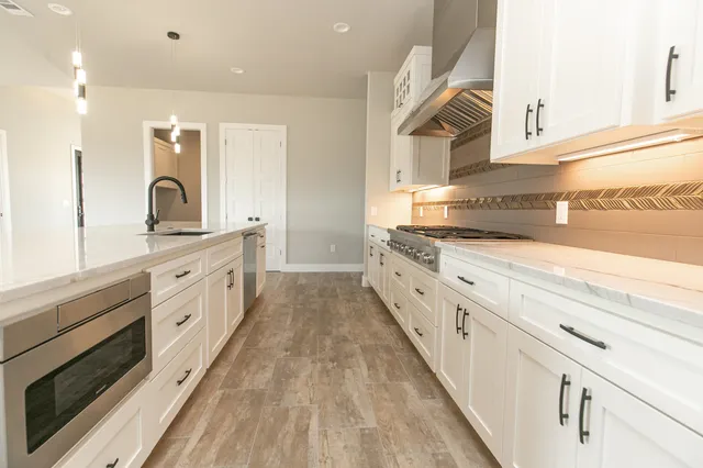 a large white kitchen with stainless steel appliances granite countertop a lot of counter space and wooden floor