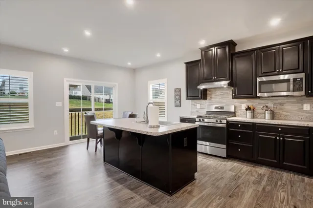 a kitchen with stainless steel appliances granite countertop wooden cabinets a sink dishwasher a stove and a refrigerator with wooden floor