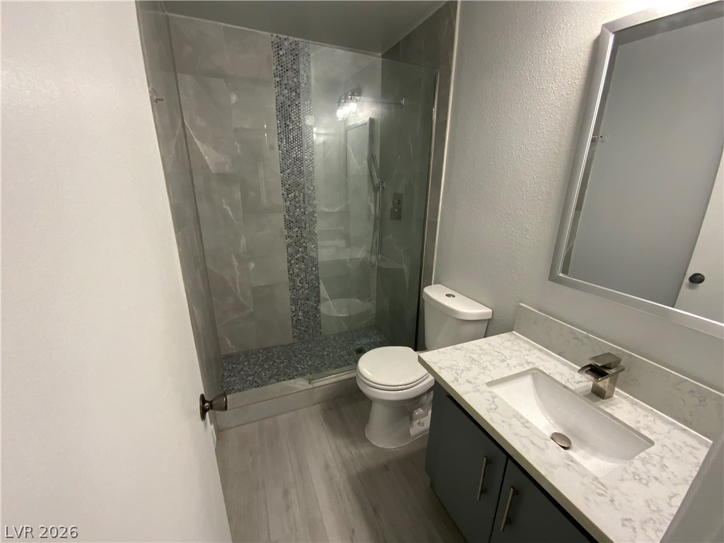 466 East Sunset Road, Unit C Henderson, NV 89011 - Photo 11 of 12 Bathroom featuring toilet, wood finished floors, tiled shower, vanity, and a textured wall