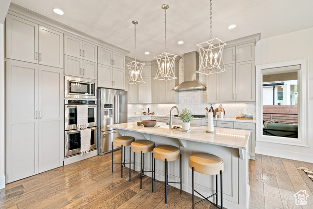 6026 Zen Trail Way St. George, UT 84790 - Photo 6 of 41 Kitchen featuring light wood-type flooring, stainless steel appliances, wall chimney exhaust hood, a breakfast bar, and a chandelier