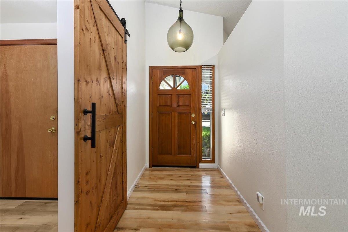9215 West Preece Street Boise, ID 83704 - Photo 2 of 22 Entryway featuring a natural wood-finish barn door, a solid wood entry door with an arched glass insert, a side light panel with blinds, a vaulted ceiling, and wood-finish flooring