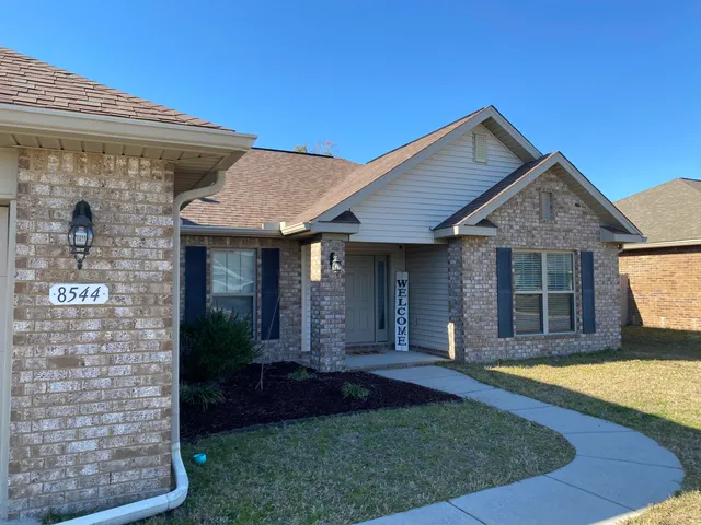 a view of a house with brick walls plants and large tree