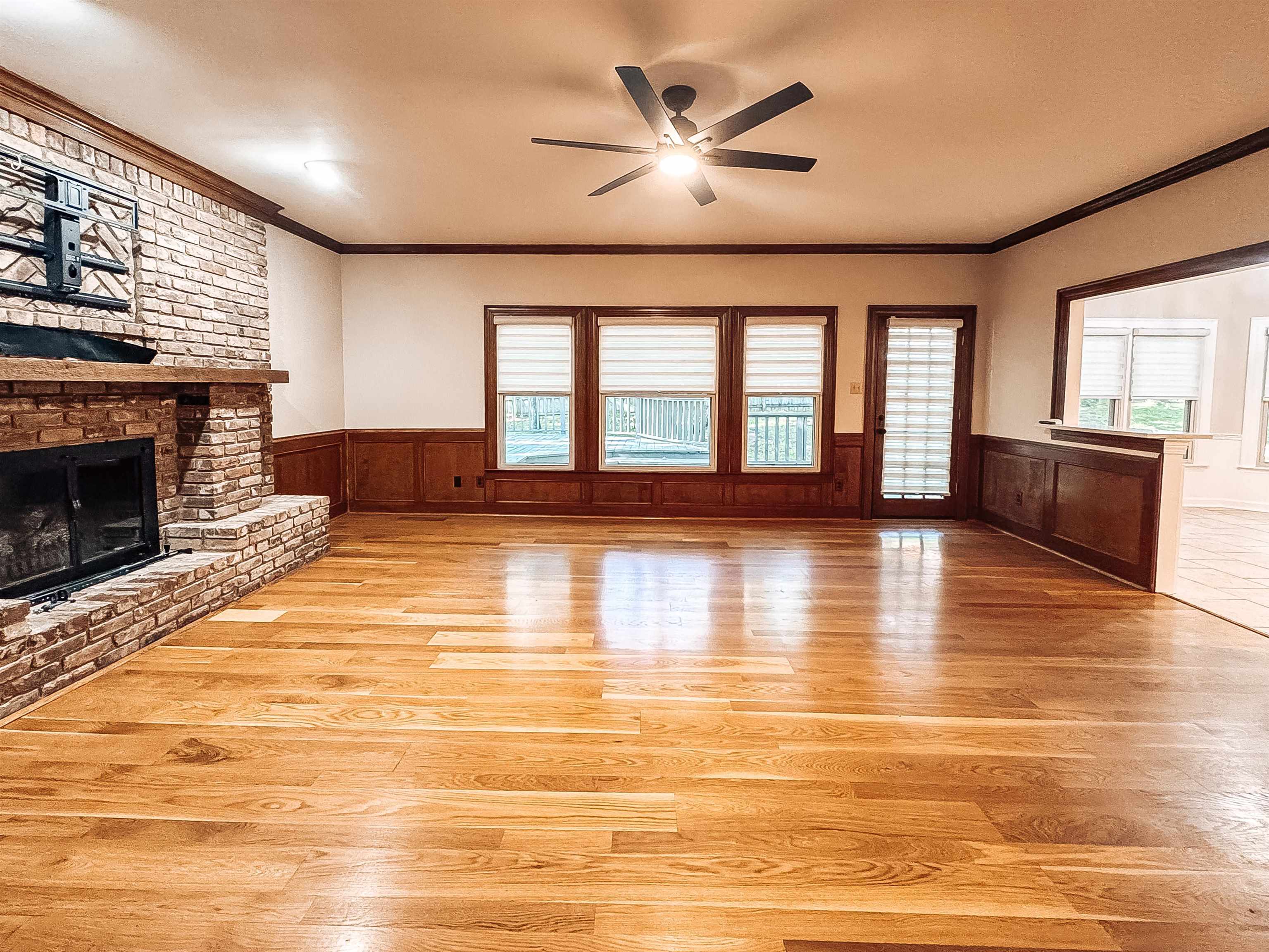 832 South Tree Drive Collierville, TN 38017 - Photo 17 of 40 Spacious living area featuring warm wood-finish flooring, a stone-clad fireplace with a hearth and mantel, dark wood wainscoting, and a ceiling fan