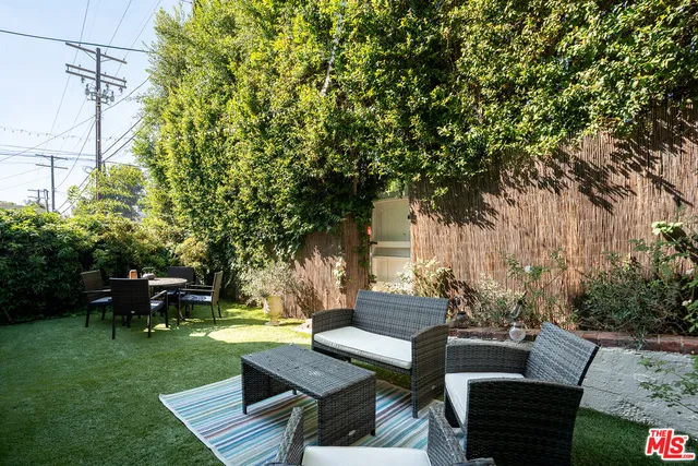 a view of a backyard with couches table and chairs with plants and trees