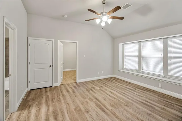 an empty room with wooden floor chandelier fan and windows