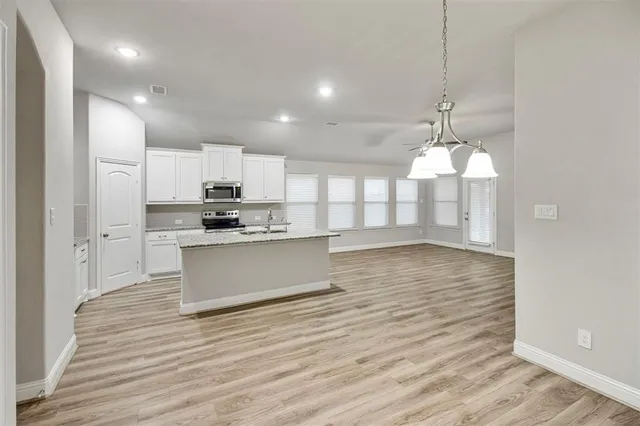 a view of a kitchen with kitchen island wooden floor stainless steel appliances and cabinets