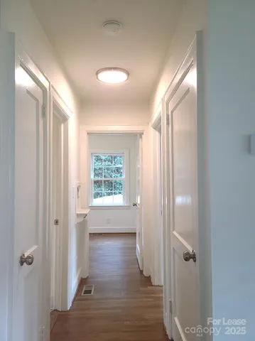a view of a hallway with wooden floor and a bathroom