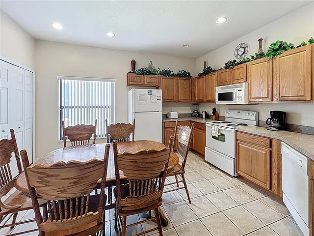 a kitchen with stainless steel appliances kitchen island granite countertop a dining table chairs and a refrigerator
