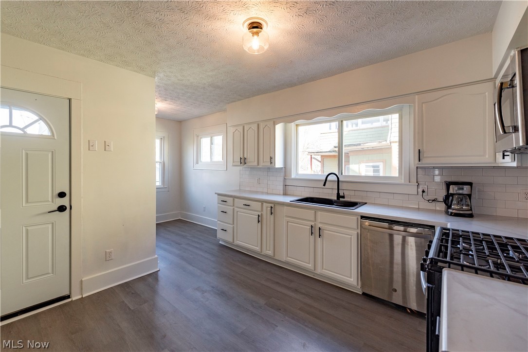 1022 North Howard Street Akron, OH 44310 - Photo 8 of 38 Beautiful while kitchen with microwave, dishwasher and gas range with stainless steel finishes, white cabinetry, subway tile backsplash, grey luxury vinyl flooring, and dark composite sink.