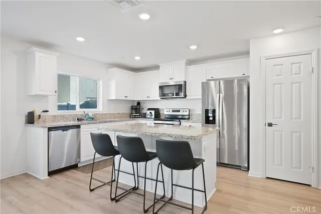 a kitchen with stainless steel appliances granite countertop a refrigerator a sink dishwasher a stove and white cabinets with wooden floor