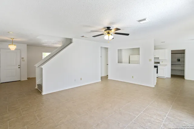 an empty room with a kitchen space and a ceiling fan
