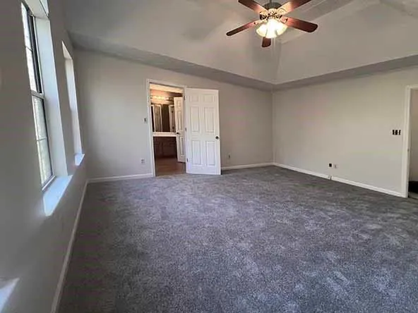 an empty room with chandelier fan and windows