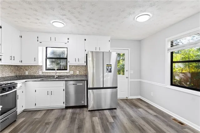 a kitchen with granite countertop a refrigerator a sink dishwasher a stove and white cabinets with wooden floor