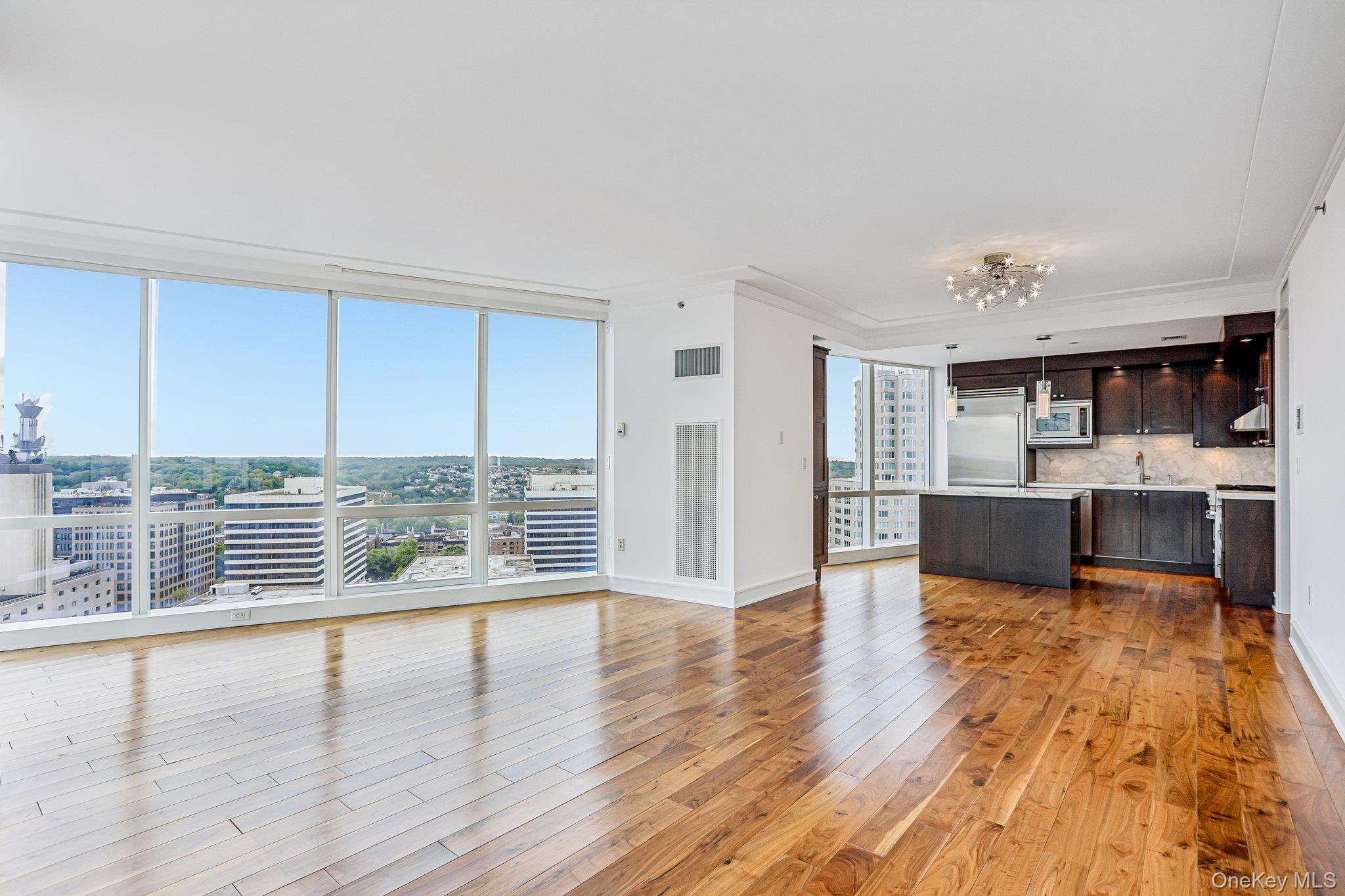1 Renaissance Square, Unit 25G White Plains, NY 10601 - Photo 3 of 22 Expansive room featuring floor-to-ceiling windows, wood-finish flooring, white walls, and elegant crown molding