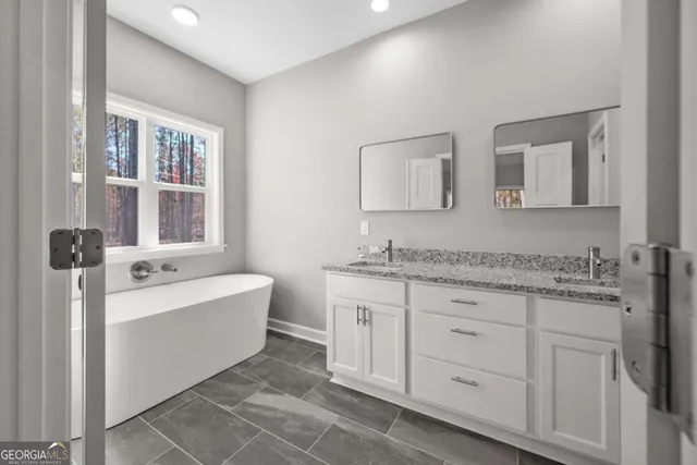 a bathroom with a granite countertop double vanity sink a mirror and a bathtub