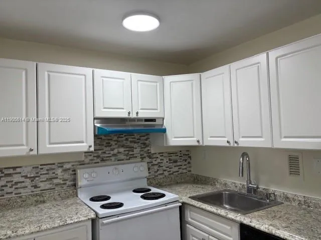 a kitchen with granite countertop a sink a stove and cabinets