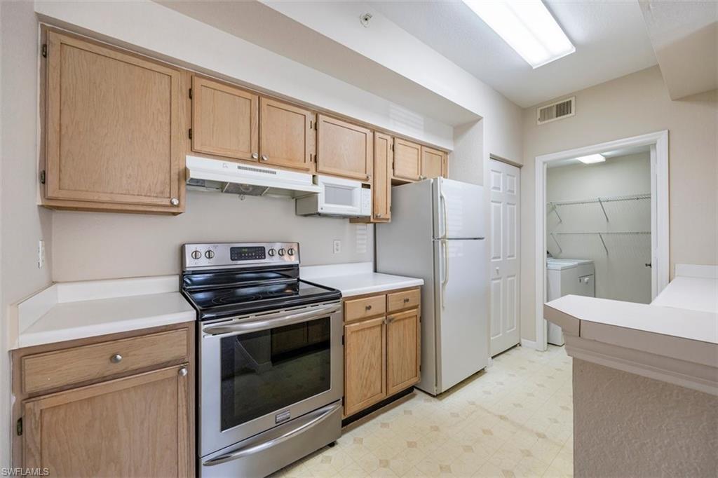 4635 St Croix Lane, Unit 1218 Naples, FL 34109 - Photo 12 of 40 Kitchen with white appliances, washing machine and clothes dryer, under cabinet range hood, light floors, and light countertops