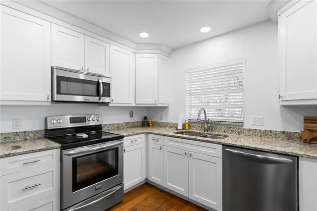 a kitchen with granite countertop white cabinets appliances a sink and a window