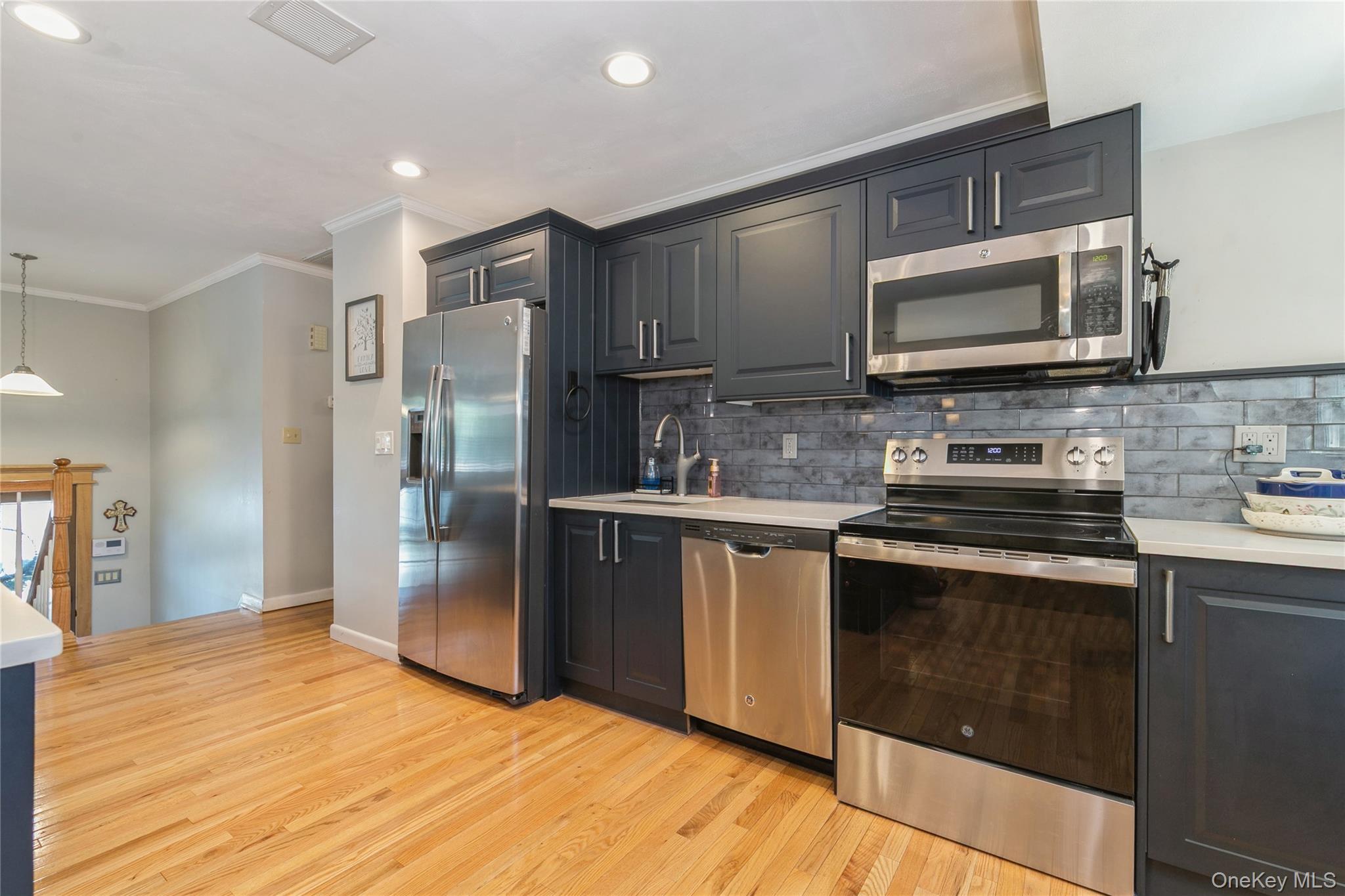 115 Clarendon Road Ronkonkoma, NY 11779 - Photo 13 of 45 Modern kitchen featuring wood-finish flooring, dark cabinetry, stainless steel appliances, light countertops, and a subway tile backsplash