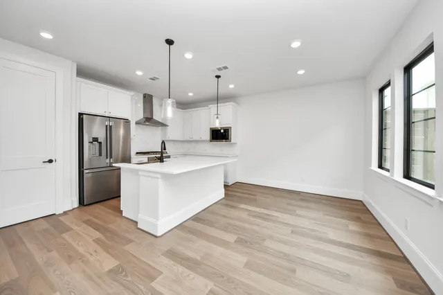 a white kitchen with stainless steel appliances kitchen island a sink a stove a refrigerator and white cabinets with wooden floor