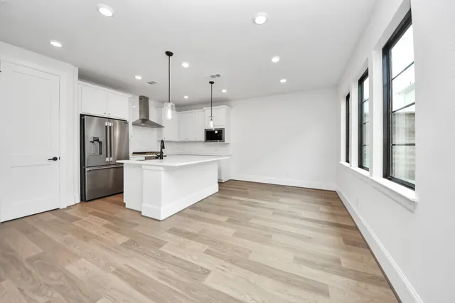 a large white kitchen with kitchen island a stove a sink dishwasher a refrigerator and white cabinets with wooden floor