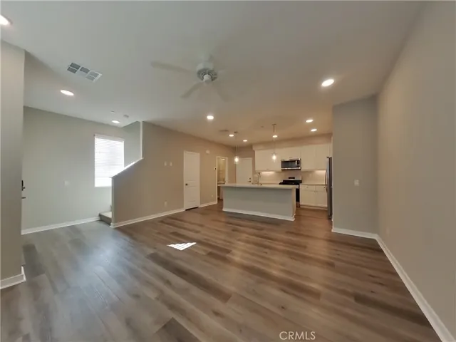 a view of an empty room with wooden floor and kitchen