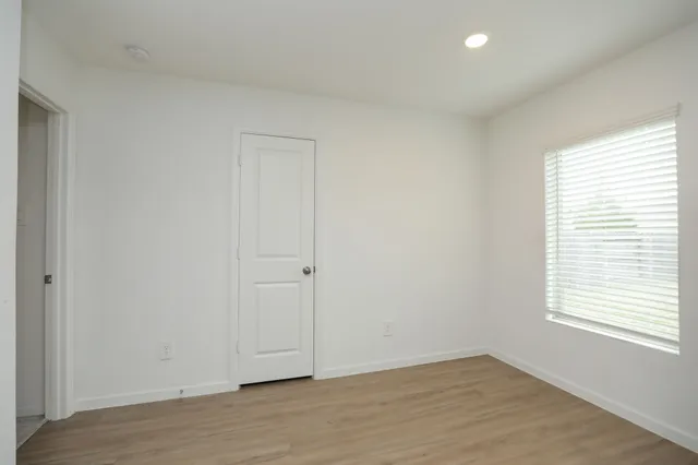 a view of an empty room with wooden floor and a window