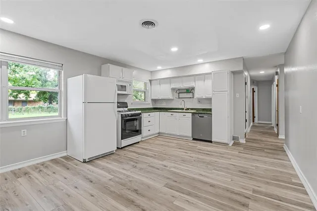 a kitchen with a refrigerator a white stove top oven and white cabinets next to a window